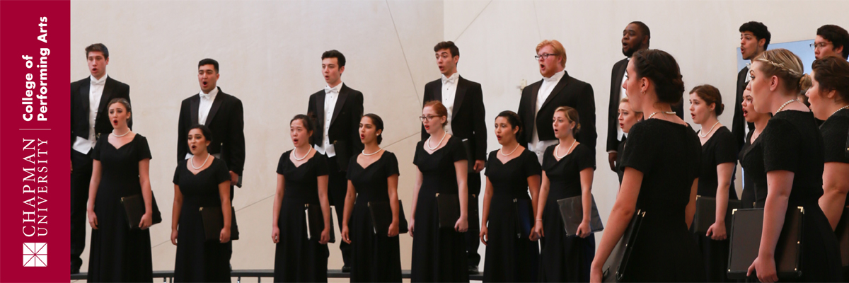 Chapman University College of Performing Ats. Singers dressed in black formal attire stand in a semicircle on rows of choral risers and sing in unison.