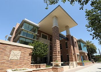 Fowler School of Engineering | Keck Center A multi-level red brick building looms tall before a clear blue skyline. Clear glass windows invite passers-by to peek inside. Palm trees and foliage line the front-face. To the left, the iconic Chapman logo, inviting all to look through the window of possibilities ahead. 